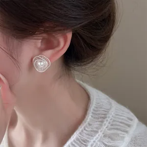 Close-up detail of elegant hollow spiral silver stud earrings with center pearl on ear