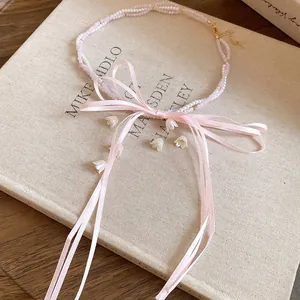 Close-up of pink ribbon bow necklace with pearl beads and lily-of-the-valley charms.