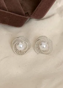 Detailed view of elegant silver hollow spiral stud earrings with white pearls on cream fabric.