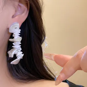 Close-up of bohemian irregular shell fringe earrings worn on model's ear for vacation style