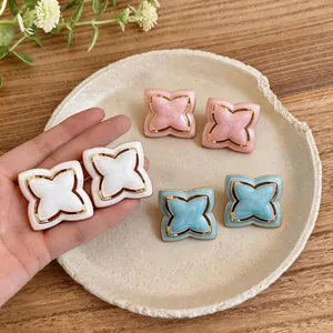 Close-up of enamel starburst flower stud earrings in white, pink, and blue with gold trim.