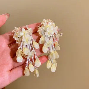 Vue détaillée des boucles d'oreilles fleurs jaunes avec glands perlés et gouttes.