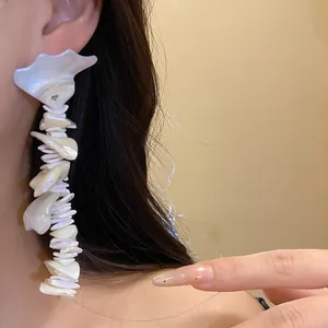 Close-up detail of Bohemian white shell tassel drop earrings worn on ear for vacation style