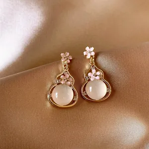 Close-up of elegant gold gourd earrings with pink flowers and white opal stones.