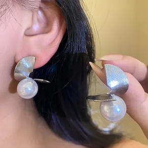 Détail de boucles d'oreilles tendance avec feuilles de métal torsadées et grandes perles blanches