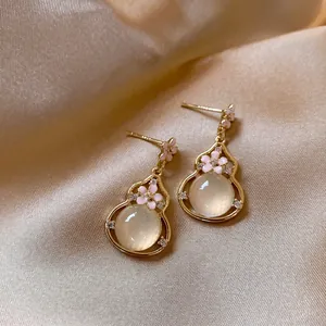 Close-up detail of elegant gold gourd pendant earrings featuring pink enamel flowers