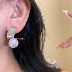 Gros plan d'élégantes boucles d'oreilles en métal argenté en forme d'éventail avec perle blanche.