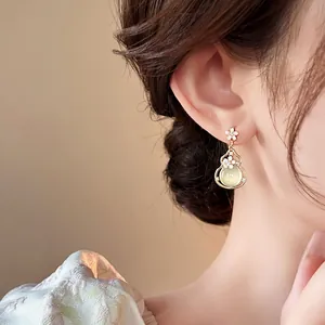Elegant gold-tone gourd dangle earrings with a pale green bead shown on a model ear