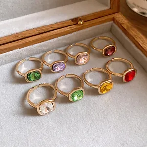 Detail view of various colorful square gemstone open rings in a wooden jewelry box.