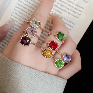 Detailed view of multiple colorful square crystal rings on fingers with a book background