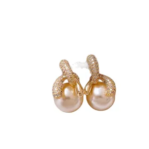 Eleganti orecchini a perno con perle e zirconi dorati su sfondo bianco