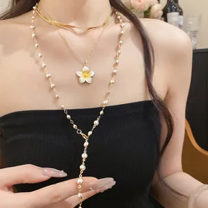 Dettaglio di una collana dorata multistrato con ciondolo a fiore e perle su modella