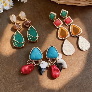 Pendientes colgantes geométricos vintage con piedras de colores y perlas sobre fondo de madera