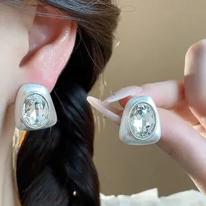 Close-up detail of geometric silver stud earrings with large oval faceted crystals
