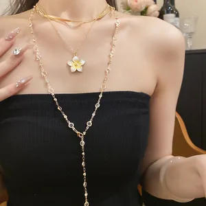 Dettaglio di una collana multistrato dorata con pendente a fiore in smalto bianco
