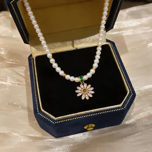 Close-up of 18k gold plated pearl necklace with zircon flower pendant in a blue box