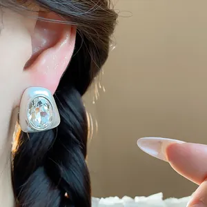 Macro view of a silver geometric earring with a large faceted crystal on a person's ear.