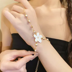 Detailed close-up of white resin flower finger bracelet with pearls on gold chain.