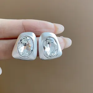Detailed macro shot of irregular matte silver stud earrings with faceted oval crystals