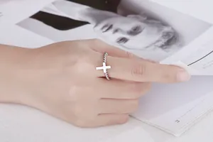 Detail shot of a minimalist silver stainless steel twisted cross ring worn on a finger.