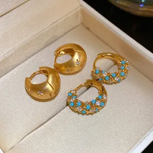 Macro view of vintage gold hoop earrings with turquoise and clear stones in a jewelry box.