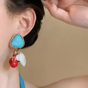 Primer plano de pendientes vintage con colgantes de concha y perla roja en modelo asiática.