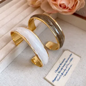 Close-up of 18K gold-plated wavy cuff bracelets with elegant marble oil-drip texture.
