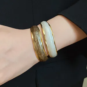 Close-up of 18K gold plated wavy bangles with olive and cream enamel inlay on wrist.