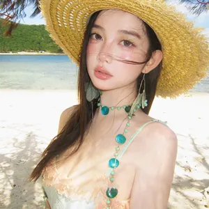 Detail view of a model wearing teal shell fringe earrings and matching beach necklace set