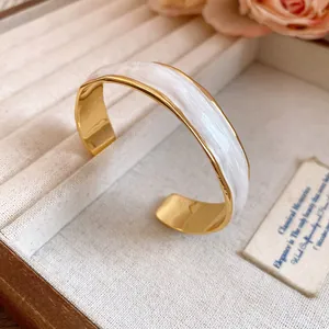 Detailed view of an 18K gold-plated open bangle featuring an elegant white wave enamel finish