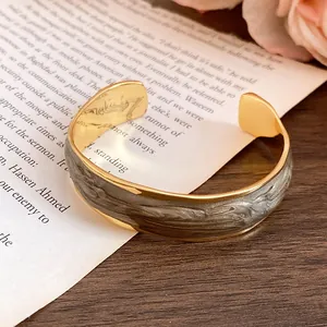 Detailed view of an 18K gold plated cuff bracelet with grey wave enamel stripes