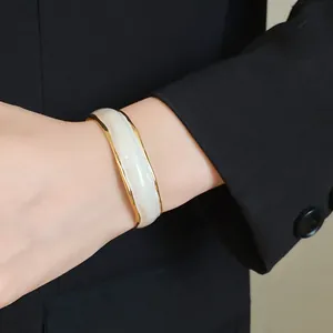 A detailed close-up of an elegant 18K gold plated wavy open bangle with white enamel