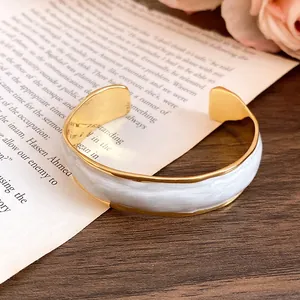 Detailed view of 18K gold-plated cuff bracelet featuring white wave enamel patterns