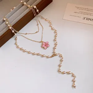 Detailansicht einer eleganten mehrlagigen Goldkette mit Perlen und einer rosa Blume