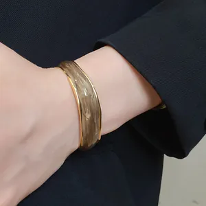 Detail view of 18K gold-plated bangle with wavy brown oil-dripped texture on model wrist.