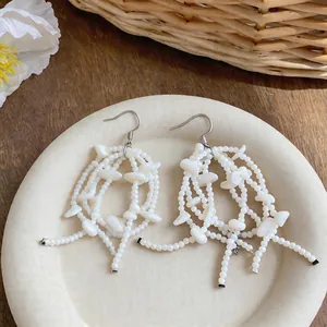 Macro detail view of elegant French style white shell bead tassel earrings on a cream plate