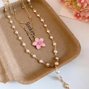 Nahaufnahme der mehrlagigen Goldkette mit rosa Blumenanhänger und Perlen auf Tablett