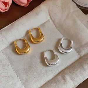 Close-up of gold and silver U-shaped hoop earrings with pleated texture