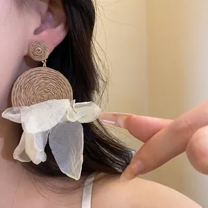 Exquisitos pendientes colgantes de rafia tejida y pétalos de gasa blanca en modelo