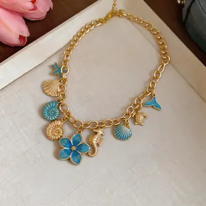 Close-up of a resort style gold chain necklace featuring blue enamel shell and seahorse pendants