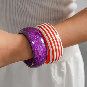 Close-up detail of trendy resin bangles featuring purple glitter stars and red stripes
