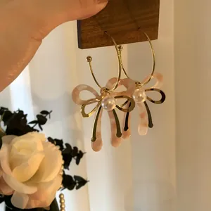 Primo piano di eleganti orecchini a cerchio a C con fiocco in acetato rosa e perle