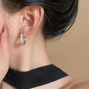 Detailed view of an elegant textured U-shaped silver hoop earring worn on model ear