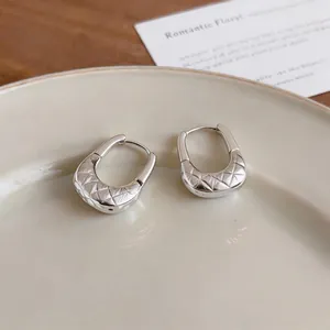 Detail view of U-shaped silver hoop earrings with quilted texture on a beige plate.