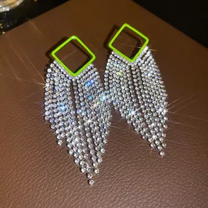 Macro view of neon green square rhinestone tassel earrings with sparkling starbursts.