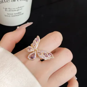 Primo piano di un anello a farfalla dorato con zirconi viola su un dito