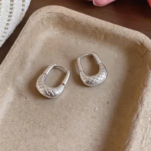 Detail shot of silver U-shaped hoop earrings with a quilted texture on a beige tray.