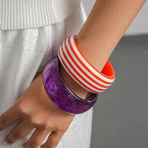 Macro detail of vibrant striped and purple glitter resin bangles worn on a model's wrist