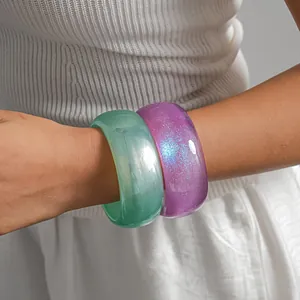 Macro view of chunky semi-transparent green and glitter purple resin bangles on wrist