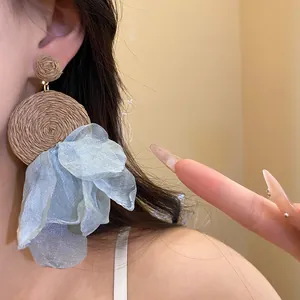 Detalle de pendientes colgantes bohemios de rafia y gasa azul claro puestos en la oreja